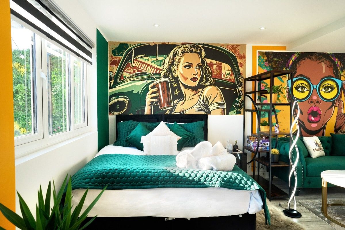 Double bed with emerald bedding beneath a retro pin-up mural